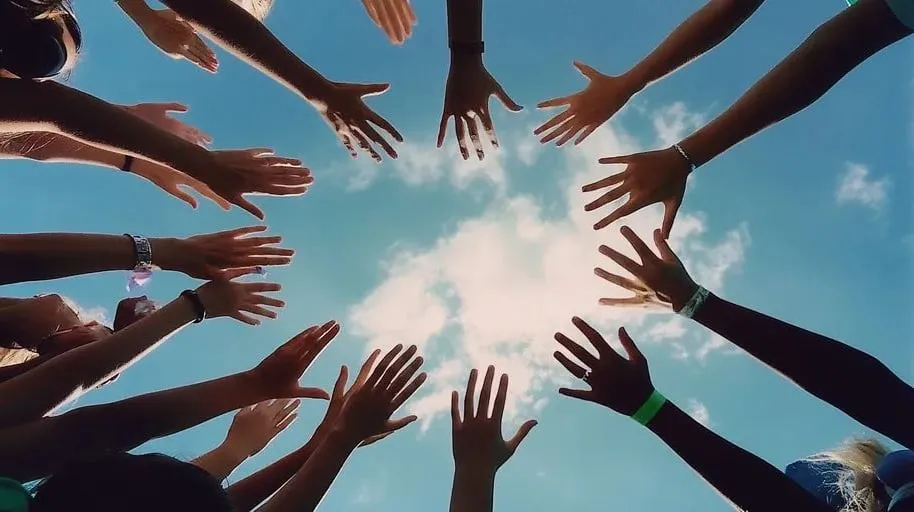 Many hands reaching toward each other in a circle against a blue sky